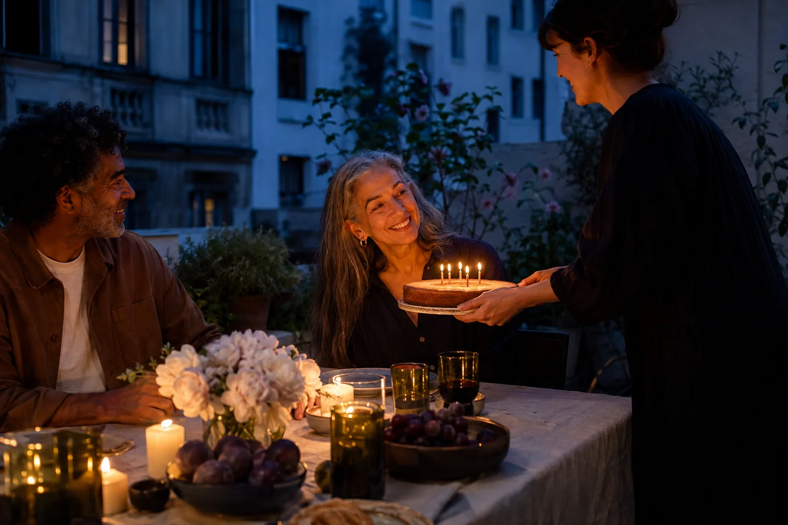 Friends sharing a birthday cake by candlelight in a courtyard at dusk.